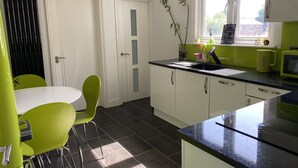 Een moderne keuken met witte kasten, een zwart aanrecht en groene stoelen.