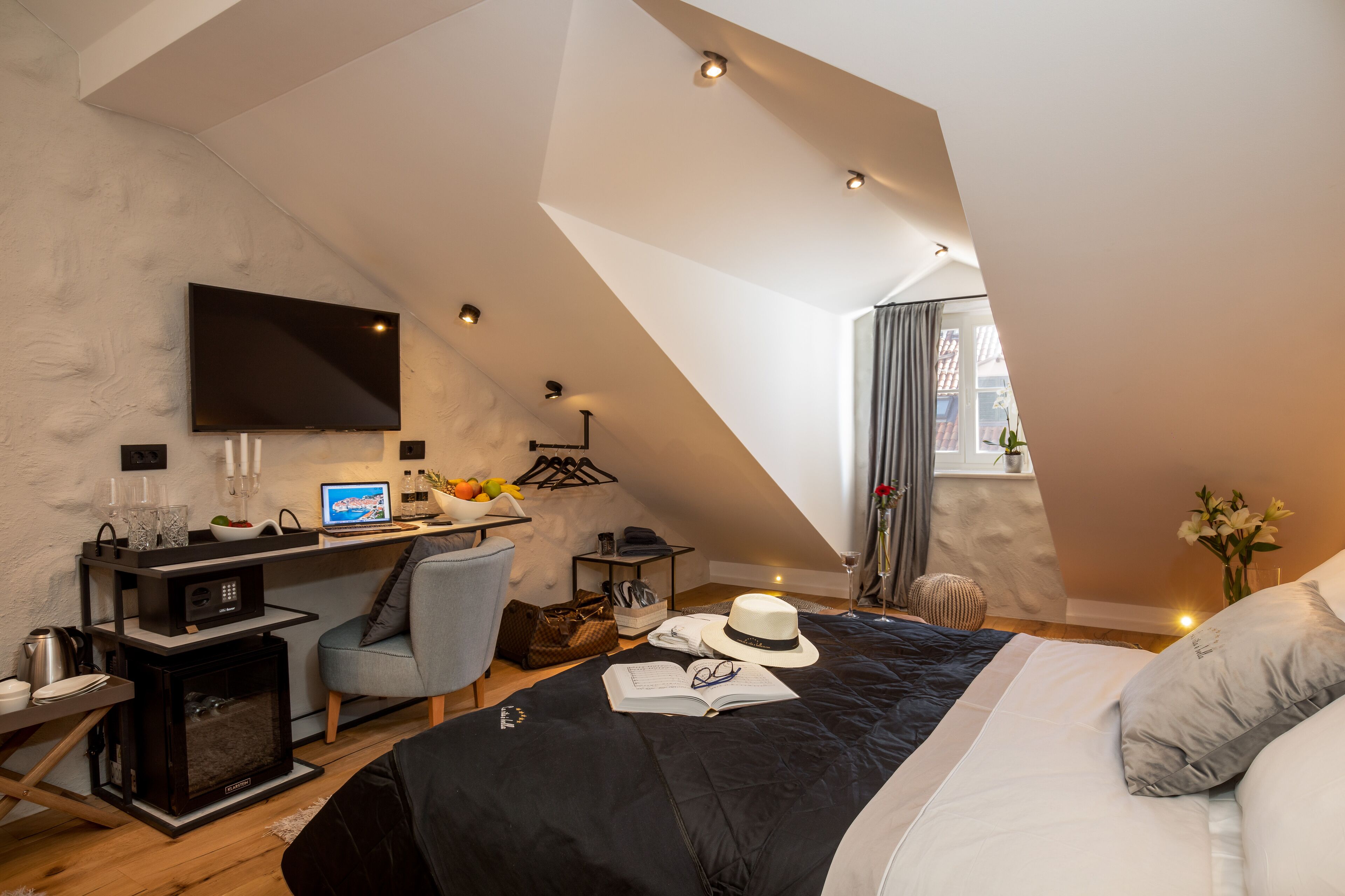 Un dormitorio moderno con techo inclinado, un televisor de pantalla plana, un escritorio con computadora y una cama cómoda con almohadas.