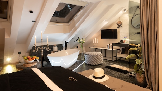 Une chambre à coucher moderne avec une lucarne, une grande baignoire et une table de chevet sur laquelle se trouve un panier de fruits.
