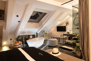 Une chambre à coucher moderne avec une lucarne, une grande baignoire et une table de chevet sur laquelle se trouve un panier de fruits.