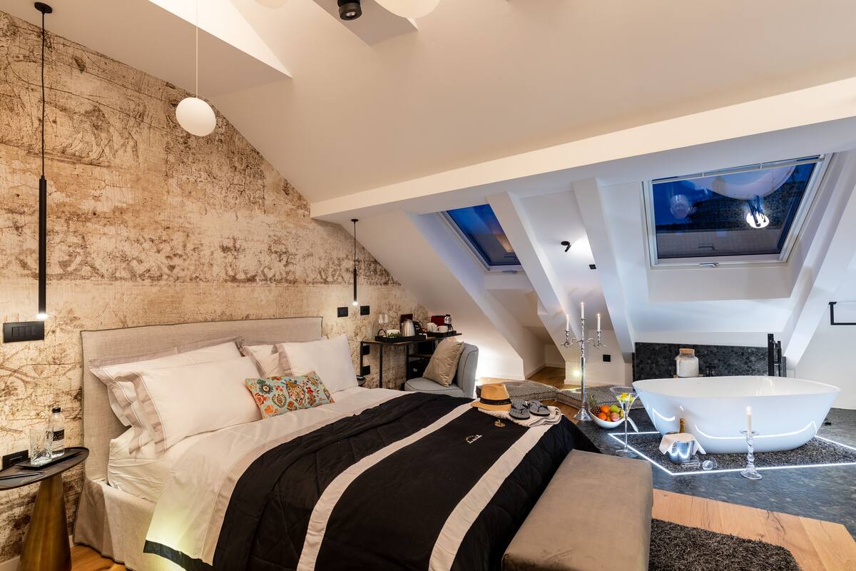 Ein modernes Schlafzimmer mit einem großen Bett, einem Oberlicht, einer Badewanne und einer kleinen Sitzecke.