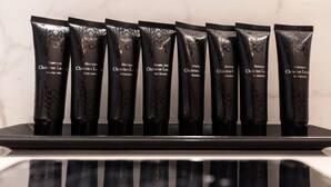 Une rangée de tubes noirs portant l’étiquette « Christian Lacroix » sur une surface réfléchissante.