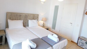 Ein Doppelbett mit Holz-Kopfstütze, zwei Kissen, ein Nachttisch mit Lampe und ein Koffer auf dem Boden.