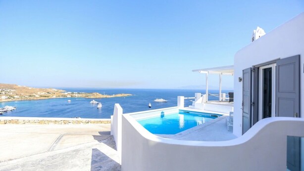 Un bâtiment blanc doté d’une piscine, qui surplombe une zone côtière où se trouvent des bateaux.