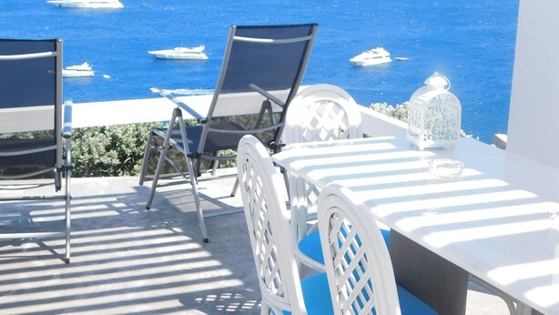 Eine Terrasse mit Tisch und Stühlen mit Blick auf das Meer, inklusive Booten und einer felsigen Küstenlinie.