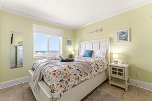 A bedroom with a bed, a bedside table, a nightstand, a window, and a wall-mounted sign.
