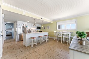 A kitchen with a central island, bar stools, a dining table with chairs, and a window with blinds. - Updated Condo - Ocean One 5N - Budget Friendly (Myrtle Beach)
