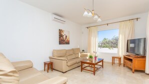 A living room with a beige sofa, a coffee table, a TV on a wooden stand, and a window with curtains.