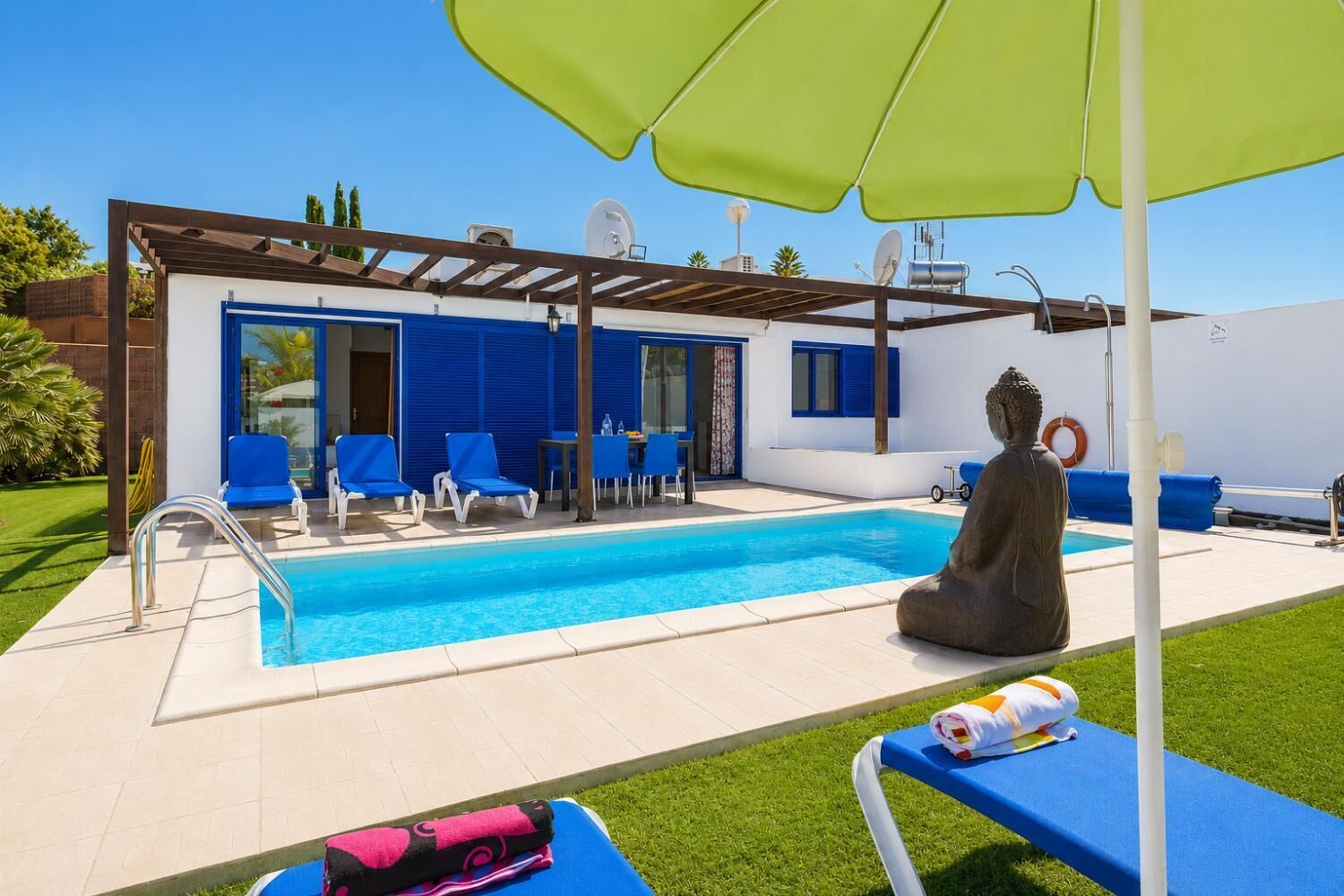 A poolside area with a statue, blue chairs, and a green umbrella.