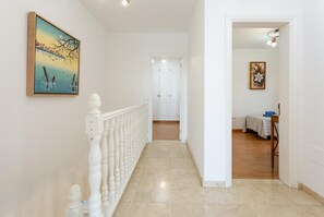 Ein Flur mit weißer Geländer, einem Gemälde an der Wand und einer Tür zu einem Zimmer mit Bett und Tisch.