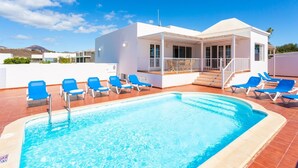 A pool area with blue lounge chairs and a white building with a covered deck.
