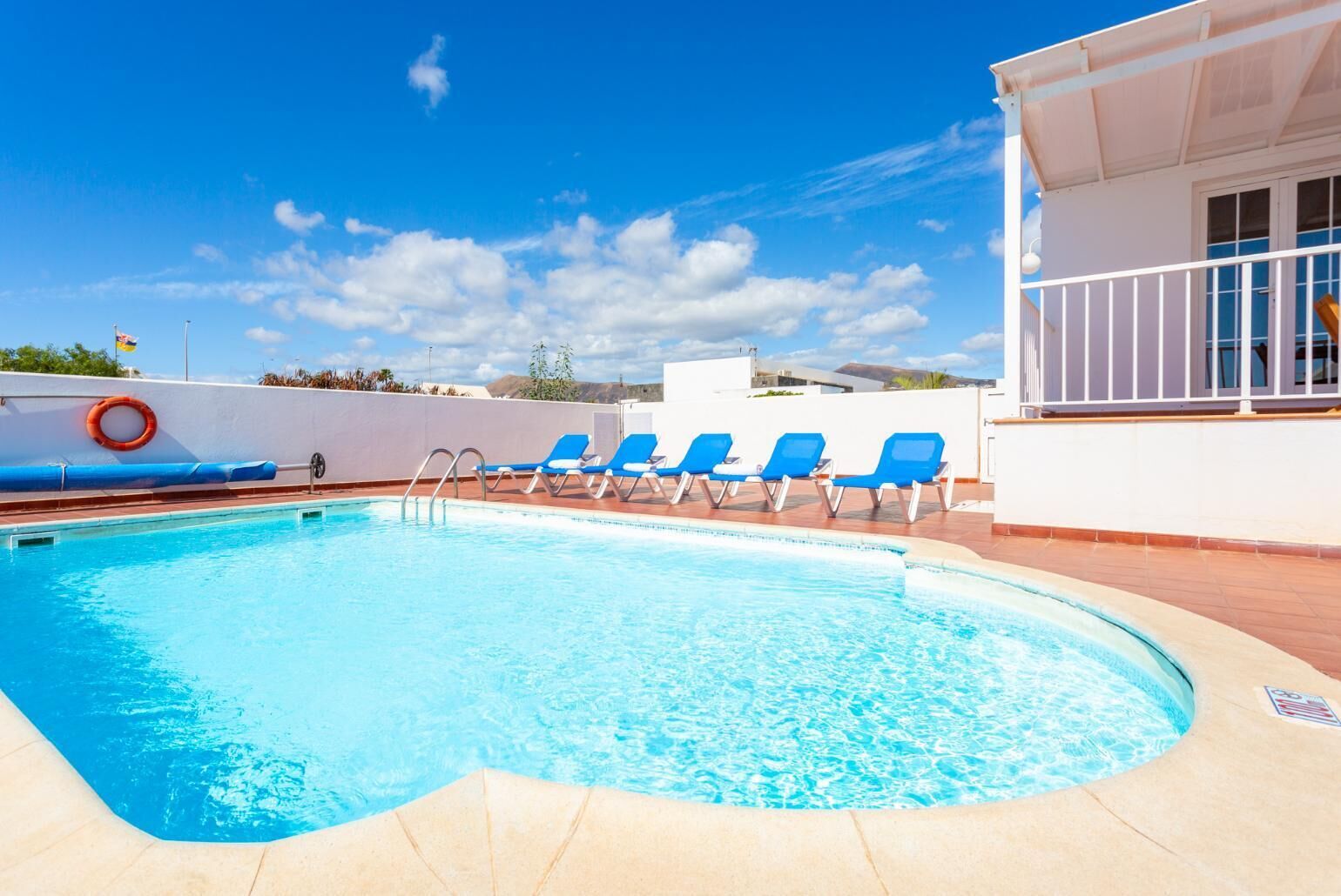 A swimming pool with blue lounge chairs and a lifebuoy, surrounded by a white building with a balcony.