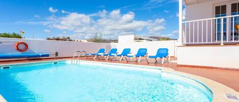 A swimming pool with blue lounge chairs and a lifebuoy, surrounded by a white building with a balcony.