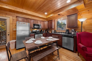 A wooden cabin kitchen with a dining table set for four, a refrigerator, microwave, stove, and dishwasher.