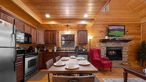 A wooden cabin interior with a kitchen, dining area, and fireplace. - Cozy Cabin: Hot Tub, Pool Table, Jacuzzi, Sleeps 8 (Pigeon Forge)