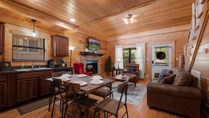 A cozy cabin interior with a wooden dining area, a fireplace, and a living room with a couch. - Cozy Cabin: Hot Tub, Pool Table, Jacuzzi, Sleeps 8 (Pigeon Forge)