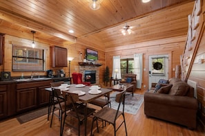 A cozy cabin interior with a wooden dining area, a fireplace, and a living room with a couch.
