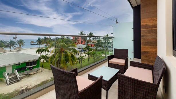 Een balkon met rieten meubilair met uitzicht op een strand en palmbomen.