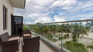 Een balkon met rieten meubels, een glazen balustrade en uitzicht op een strand met palmbomen.