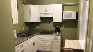 A kitchen with white cabinets, a granite countertop, a microwave, and a coffee maker.