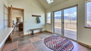 A spacious room with a large sliding glass door leading to a deck, a bench, and a patterned rug. - Spacious Farm House with Stunning Mountain Views (Joseph)