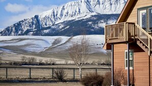 A wooden building with a balcony overlooking a snowy mountain and a fenced field. - Spacious Farm House with Stunning Mountain Views (Joseph)