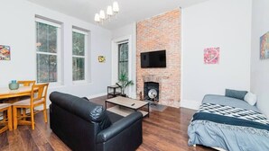 A modern living room with a fireplace, a black sofa, a dining table with chairs, and a bed with a patterned blanket. - Business Suite  - Walkable Entertainment (Pittsburgh)