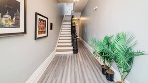 A hallway with a staircase, framed pictures on the walls, and potted plants. - Business Suite  - Walkable Entertainment (Pittsburgh)