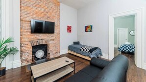 A room with a brick fireplace, a bed with a blue and white patterned bedspread, a black sofa, and a wooden coffee table. - Business Suite  - Walkable Entertainment (Pittsburgh)