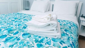 Cama bem arrumada com colcha florida e uma pilha de toalhas brancas.