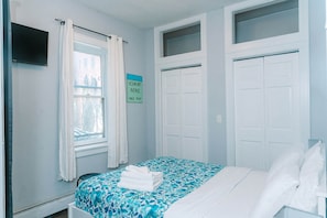 Habitación de hotel con cama, ventana con cortinas, cartel con el precio de la habitación y puertas blancas.