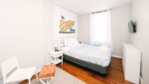 Ein Schlafzimmer mit einem Bett, einem Sessel, einem Schreibtisch, einem Fernseher und einem Bild an der Wand.