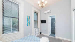 A bedroom with a bed, a TV, a shower, and a door leading to a bathroom. - Spectacular Location - Walkable Entertainment (Pittsburgh)