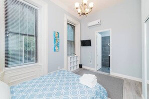 A bedroom with a bed, a TV, a shower, and a door leading to a bathroom.