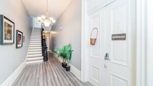 A hallway with a staircase, a welcome sign, a basket, and potted plants. - Spectacular Location - Walkable Entertainment (Pittsburgh)
