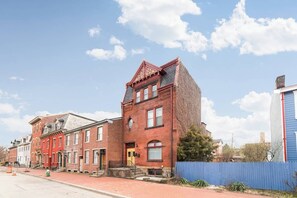 Una hilera de casas urbanas de ladrillo rojo con una valla azul, cielo despejado y acera de ladrillo rojo.