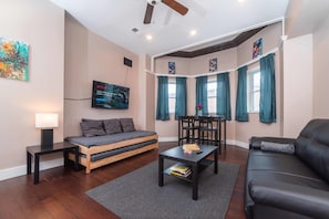A modern living room with a sofa, a coffee table, a TV, and a dining area with chairs and a table.