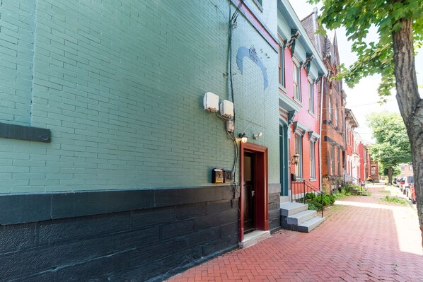 A brick building with a green facade, a red door, and a brick-paved street.