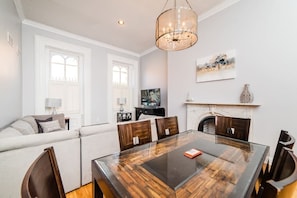 A dining area with a glass-top table, wooden chairs, a chandelier, a fireplace, and a sofa with cushions.