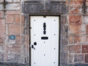 A white door with a brass knocker, a small plaque with the number 36, and a black mail slot.