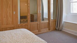 Ein Schlafzimmer mit einem Holzschrank, einem Bett mit floralem Überwurf und einem Fenster mit Vorhängen.