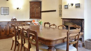 Ein Esszimmer mit einem großen Holztisch, umgeben von Stühlen, einer Blumenvase und einem Kamin.
