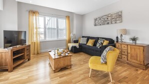 A living room with a TV, wooden furniture, a sofa, and a yellow armchair. - Eleven Popeshead - 2 bed, 2 bath central apartment (York)