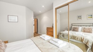 A modern bedroom with two beds, a wooden dresser, and a large mirror. - Eleven Popeshead - 2 bed, 2 bath central apartment (York)