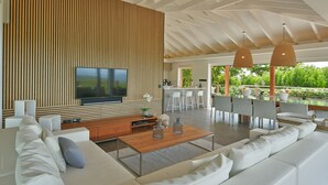 Una sala de estar moderna con un televisor de pantalla plana grande, sofás blancos, una pared de acento de madera y una zona de comedor con taburetes de bar.