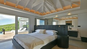 Un dormitorio moderno con una cama grande, un baño y un balcón con vistas al verdor.