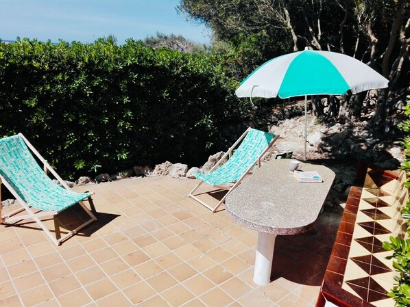Eine Terrasse mit zwei Liegestühlen, einem Tisch und einem türkisfarbene und weißen Sonnenschirm.