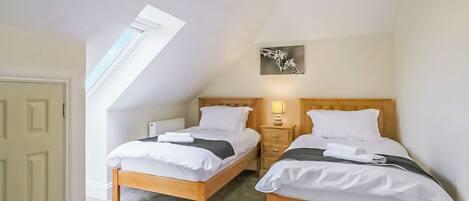A room with two wooden beds, a small bedside table with a lamp, a radiator, and a skylight.