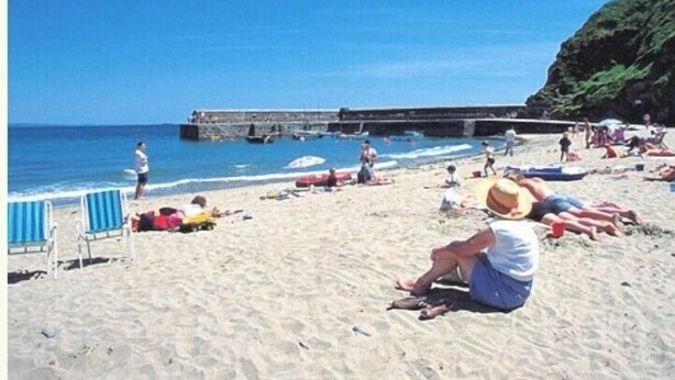 Ein Strand mit sonnenbadenden Menschen, ein Pier im Hintergrund und ein klarer, blauer Himmel.