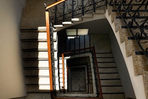 A staircase with a wooden handrail and black metal balusters, leading to a landing with a patterned door. - EL Colonial Hotel Open Bar Adults Only (San Juan)